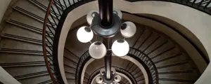 a spiral staircase photographed in Turin, Italy, in a historic building; a descending flight of stairs filled with lights, a spiral staircase photographed in Turin, Italy, in a historic building; a descending flight of stairs filled with lights,
