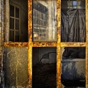 Rusted industrial window divided into six panes, each framing a different glimpse of an abandoned interior: doors, dark tarps and surfaces worn by time Rusted industrial window divided into six panes, each framing a different glimpse of an abandoned interior: doors, dark tarps and surfaces worn by time