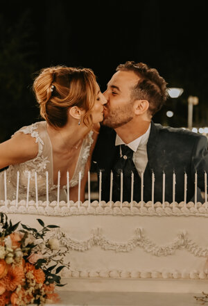 Bacio degli sposi dietro la torta nuziale decorata con fiori e candele