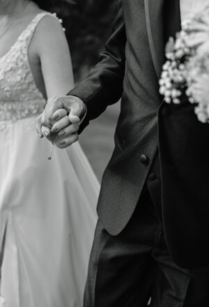 Dettaglio in bianco e nero delle mani intrecciate degli sposi e del bouquet