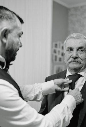 Lo sposo sistema la cravatta a un uomo durante i preparativi del matrimonio, in bianco e nero
