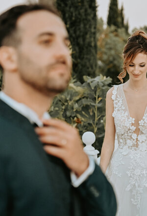 Lo sposo sistema la cravatta mentre la sposa si avvicina lungo un viale alberato