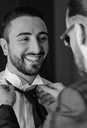 Lo sposo sorride mentre un uomo gli sistema la cravatta prima del matrimonio
