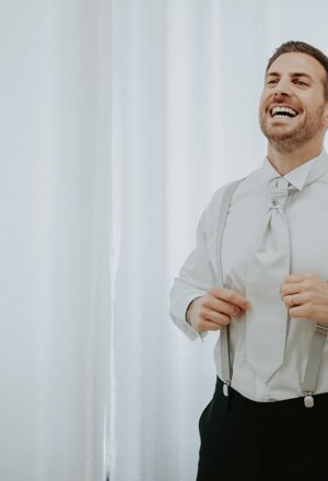Lo sposo sorride mentre sistema le bretelle durante i preparativi del matrimonio