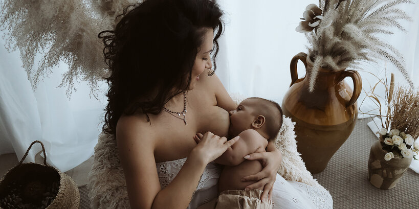 Mamma serena allatta dolcemente il suo bambino, avvolta dalla luce calda e naturale dello studio fotografico