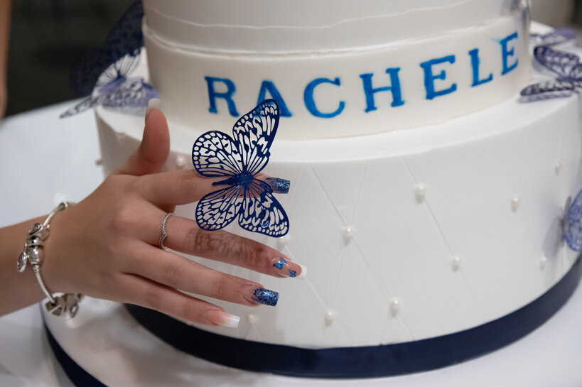 Elegante torta di compleanno bianca per i 18 anni, con una ragazza che avvicina la mano e una farfalla blu posata sul suo dito indice durante la festa