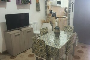 Zona giorno con TV, sedie bianche e cucina attrezzata, Villetta Marisella a Pachino