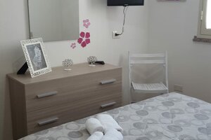 Camera con letto grigio, cassettiera in legno chiaro e specchio con decorazioni floreali, Villetta Marisella a Pachino