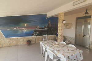 Patio coperto con tavolo, sedie bianche e murales marino al tramonto, Villetta Marisella a Pachino