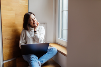 tender-woman-is-working-her-laptop-while-sitting-wide-windowhill-daily-time