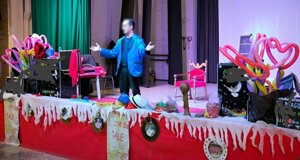 Animazione per bambini con mago su palco decorato con palloncini a forma di cuore, cappelli colorati e scenografia vivace