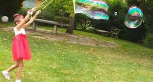 Bambina in abito rosso gioca con bolle di sapone enormi in giardino