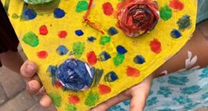 Bambino con cuore decorato con macchie colorate e fiori di carta, animazione creativa per bambini