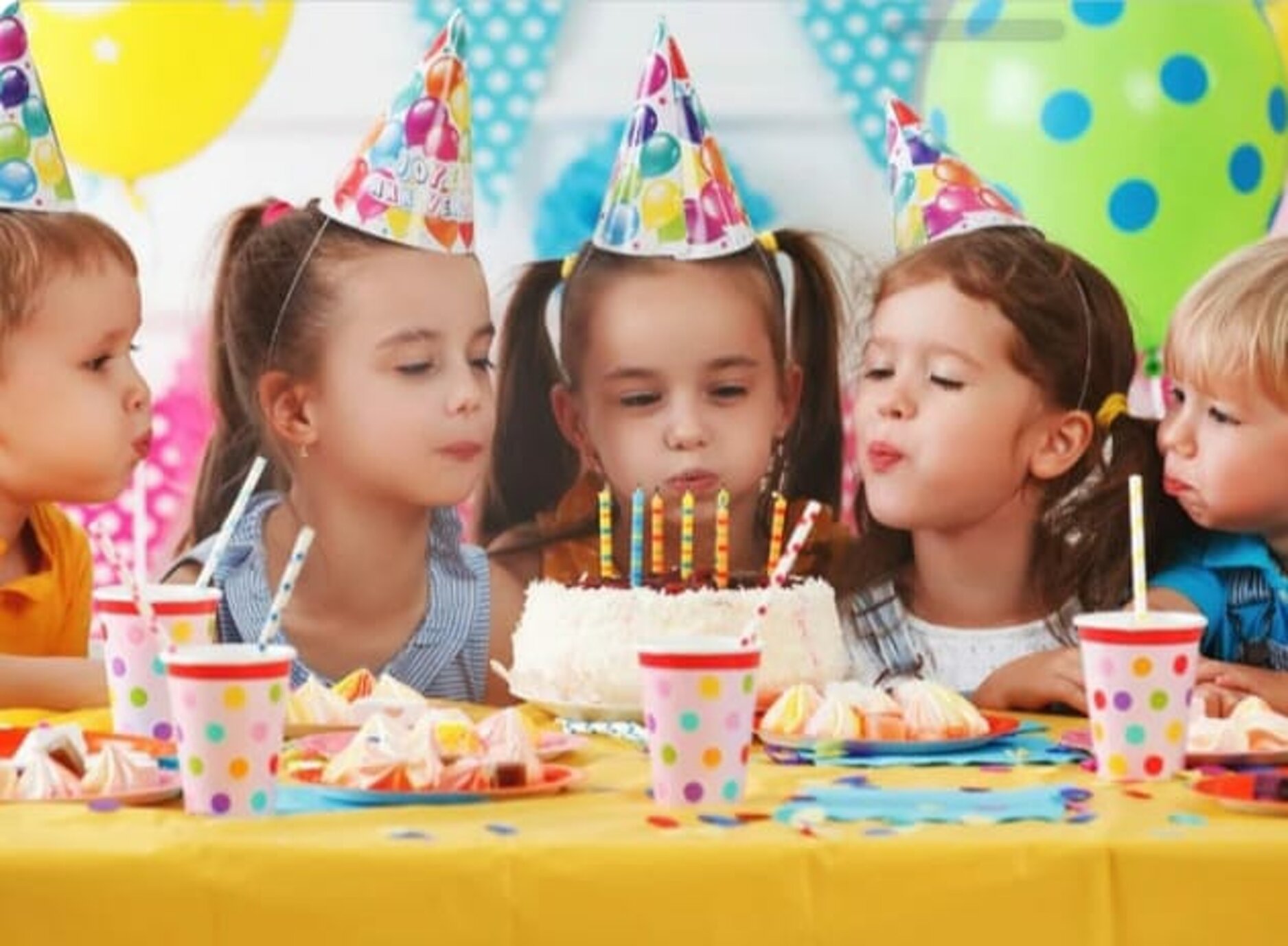 Bambini che soffiano sulle candeline durante una festa di compleanno con cappelli colorati.