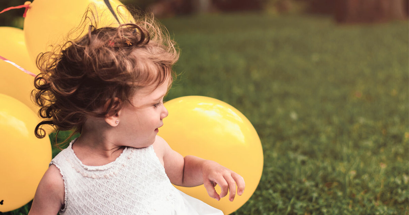 Bambina con palloncini gialli su prato verde