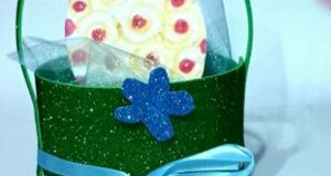 Regalo creativo con biscotto decorato dentro una scatola verde con nastrino blu, ideale per eventi speciali.