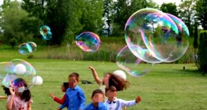 Bambini giocano all'aperto con bolle di sapone in un prato verde