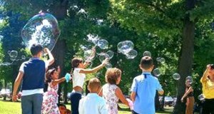 Bambini che giocano con bolle di sapone in un parco durante una festa di compleanno.