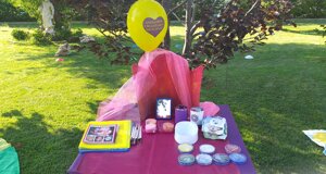 Tavolo allestito per animazione creativa in giardino, con materiali per face painting e un palloncino giallo.