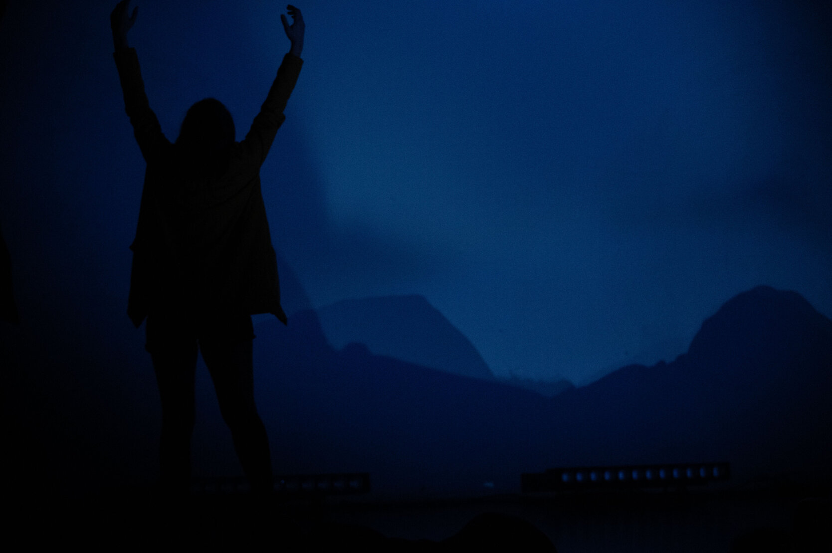 Dancer silhouette raising arms against a blue stage projection