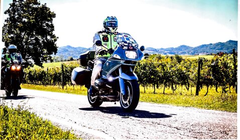 Motociclista in giubbotto giallo seduto su moto con pacchi, vicino a un veicolo dell'Esercito Italiano