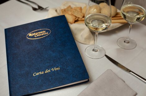 carta dei vini su tavolo apparecchiato con calici di vino bianco