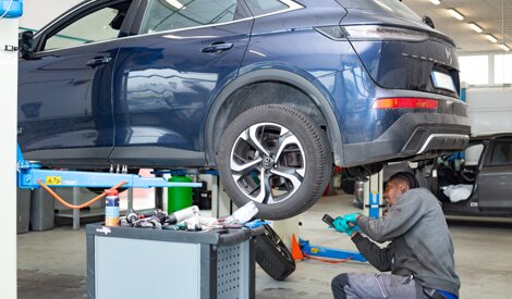 Meccanico esegue un controllo sotto l'auto sul ponte in officina