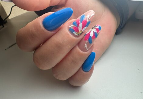 mano femminile mostra la ricostruzione unghie e lo smalto azzurro con decorazioni colorate che ricordano i fiori