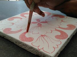 Hand painting a Sicilian tile with red floral design, showcasing handcrafted ceramics and Mediterranean design.