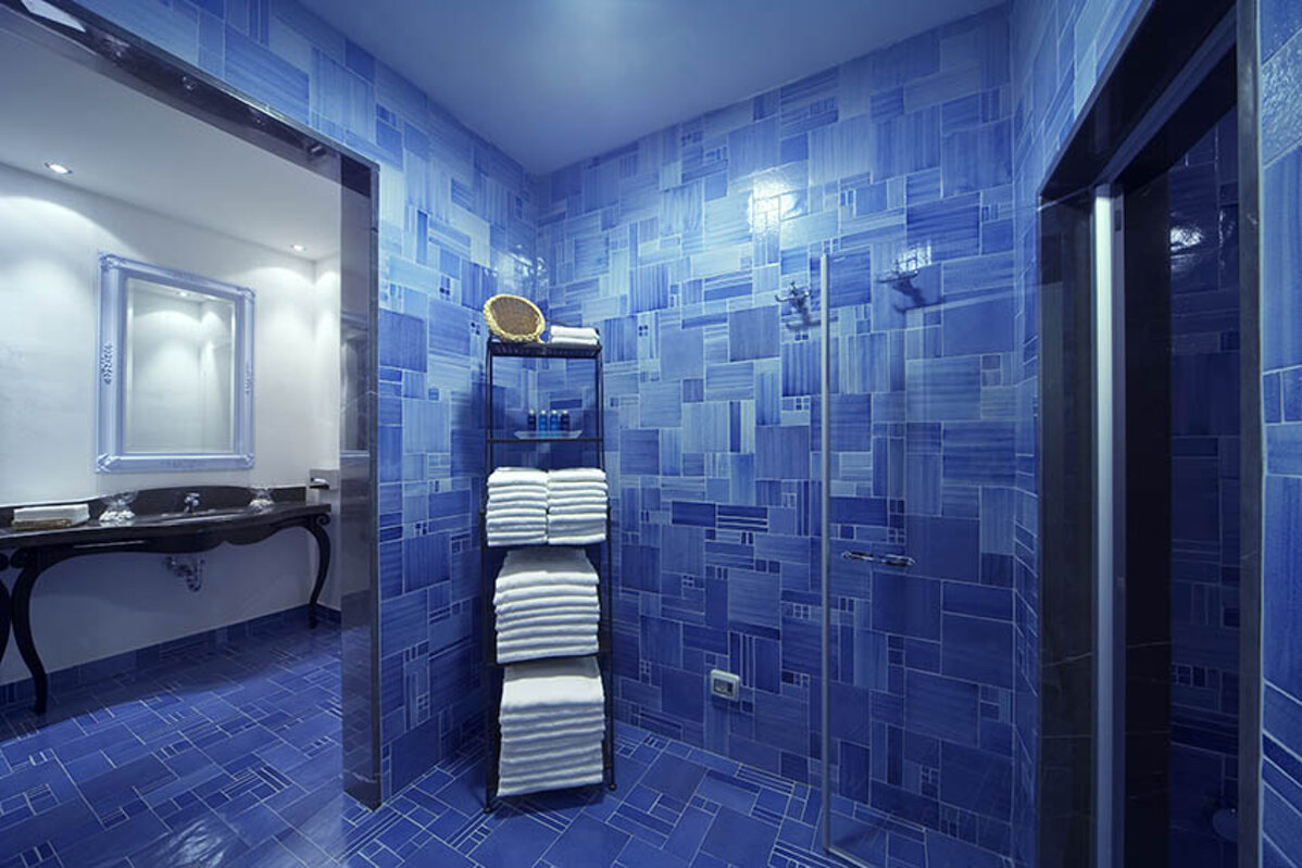 Modern bathroom with blue tiled walls and floor, featuring a glass shower and neatly stacked towels.