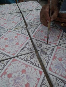 Artisan painting Sicilian tiles with floral patterns, showcasing handcrafted ceramics and Mediterranean design.