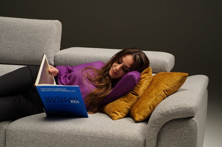 Donna rilassata su divano letto con libro, comfort e artigianalità Made in Italy
