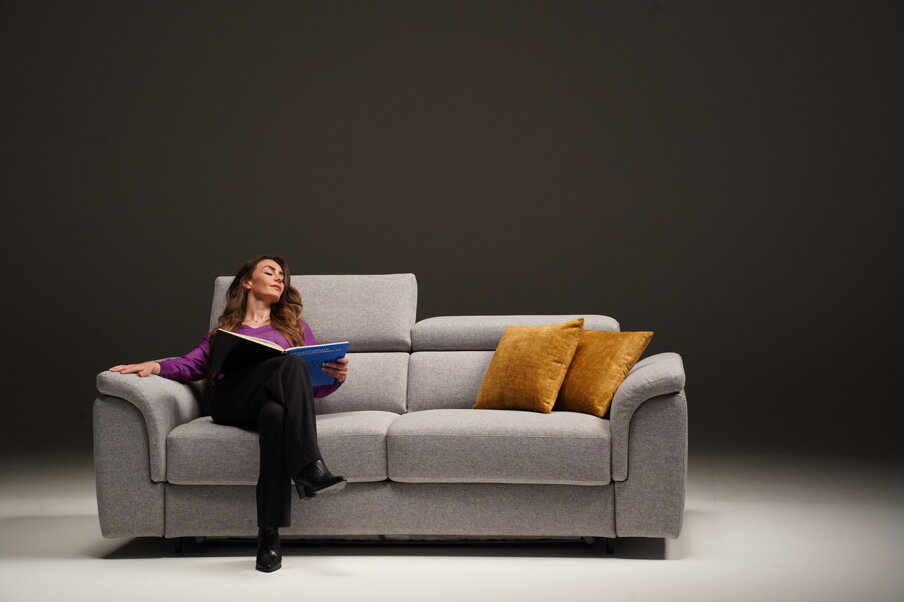 Donna rilassata su un divano letto grigio con cuscini gialli, leggendo un libro
