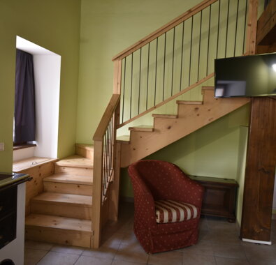 Interno di un appartamento vacanze con soggiorno dotato di scala in legno, pareti verdi e poltrona rossa. Interno di un appartamento vacanze con soggiorno dotato di scala in legno, pareti verdi e poltrona rossa.