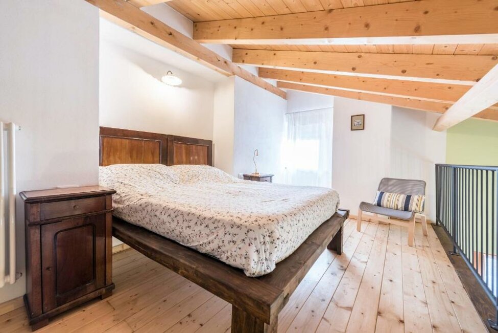 Camera da letto luminosa con travi a vista, letto matrimoniale e pavimento in legno