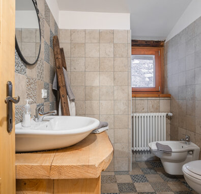 Bagno moderno con lavabo in ceramica e bidet, rivestimenti in piastrelle beige e finestra in legno