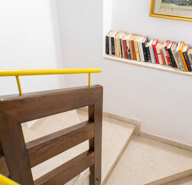 Scala interna con corrimano in legno e giallo, mensola con libri e quadro decorativo Scala interna con corrimano in legno e giallo, mensola con libri e quadro decorativo