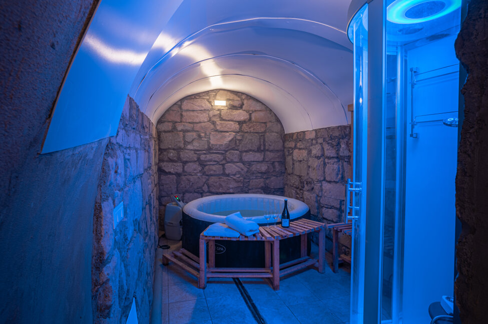 Vasca idromassaggio in un ambiente con pareti in pietra, illuminazione blu soffusa