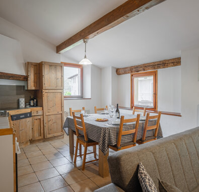 Cucina e sala da pranzo in un appartamento con travi in legno e tavolo apparecchiato.