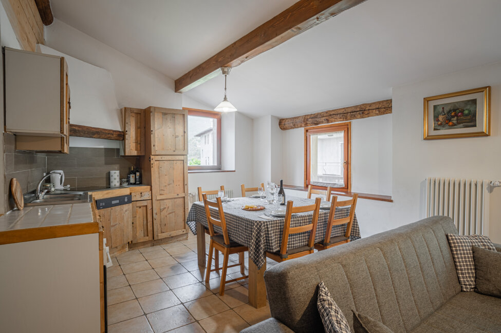 Sala da pranzo accogliente con tavolo apparecchiato, cucina rustica in legno e finestre luminose.