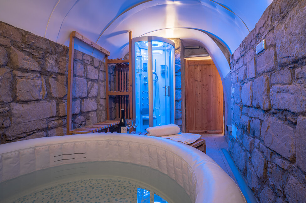 Spa privata con vasca idromassaggio in pietra e doccia moderna illuminata di blu.