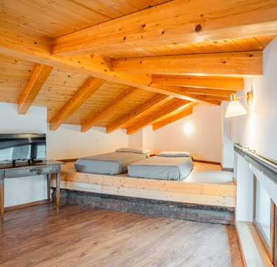 Mansarda con travi in legno, letti su pedana, TV moderna Mansarda con travi in legno, letti su pedana, TV moderna