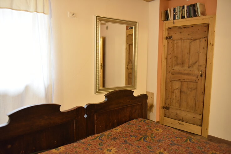Interno di una camera da letto rustica con specchio, testiera in legno e porta di legno antica, Appartamento Rosso. Interno di una camera da letto rustica con specchio, testiera in legno e porta di legno antica, Appartamento Rosso.