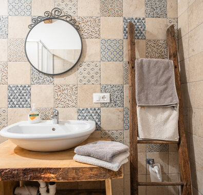 Bagno con lavabo moderno, specchio rotondo e parete con piastrelle decorative