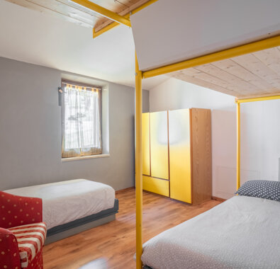 Camera da letto moderna con letti singoli, armadio giallo e poltrona rossa, pavimento in legno chiaro Camera da letto moderna con letti singoli, armadio giallo e poltrona rossa, pavimento in legno chiaro