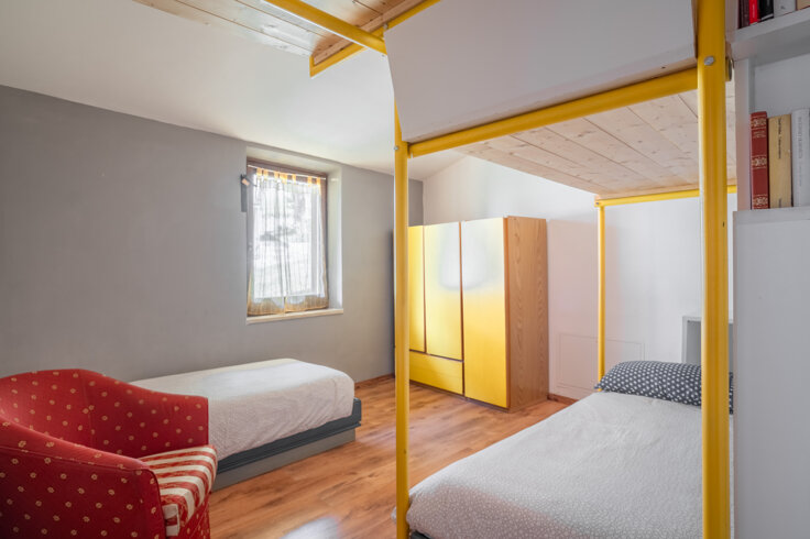 Camera da letto luminosa con due letti singoli, armadio giallo e poltrona rossa Camera da letto luminosa con due letti singoli, armadio giallo e poltrona rossa