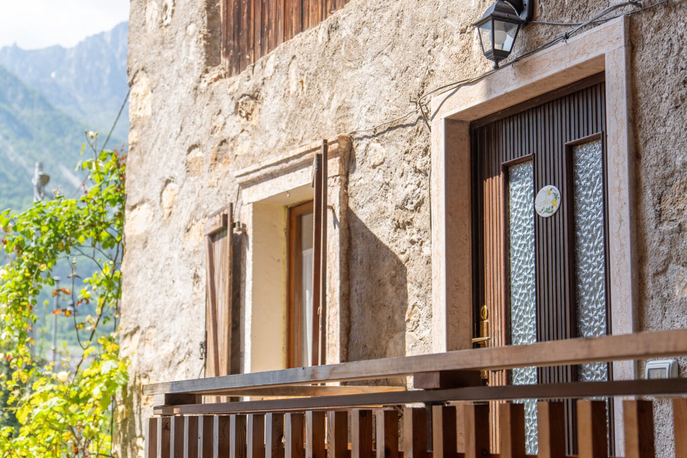 Facciata di una casa in pietra con finestra e porta in legno, immersa nella natura a Tenno
