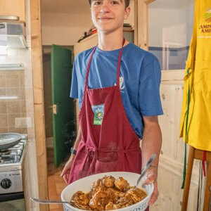Giovane in cucina con grembiule rosso che tiene un piatto di arrosti Giovane in cucina con grembiule rosso che tiene un piatto di arrosti