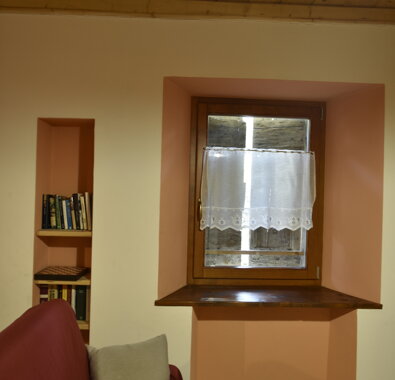 Interno di appartamento con divano rosso, finestra con tendina e libreria a muro Interno di appartamento con divano rosso, finestra con tendina e libreria a muro