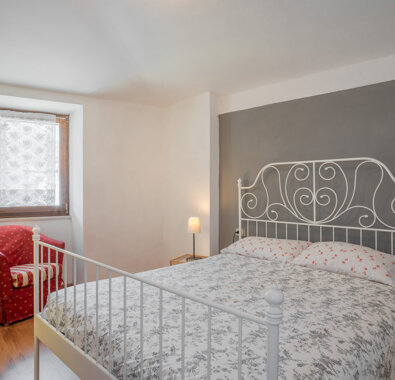 Camera da letto accogliente con letto matrimoniale in ferro battuto, poltrona rossa, e abat-jour Camera da letto accogliente con letto matrimoniale in ferro battuto, poltrona rossa, e abat-jour